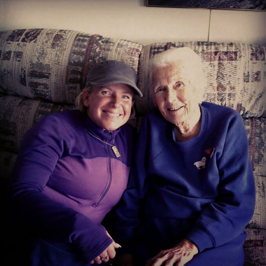 Amanda and Dot sit close together on a patterned sofa, smiling at the camera.